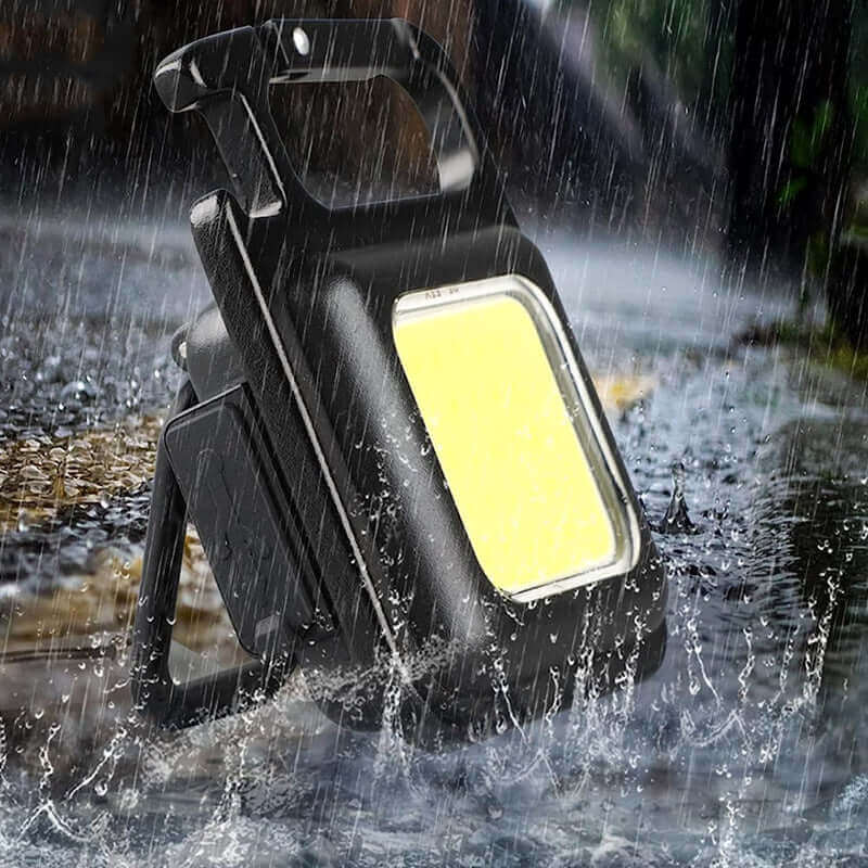 Mini waterproof pocket torch LED keychain flashlight in heavy rain, ideal for outdoor lighting and emergencies.